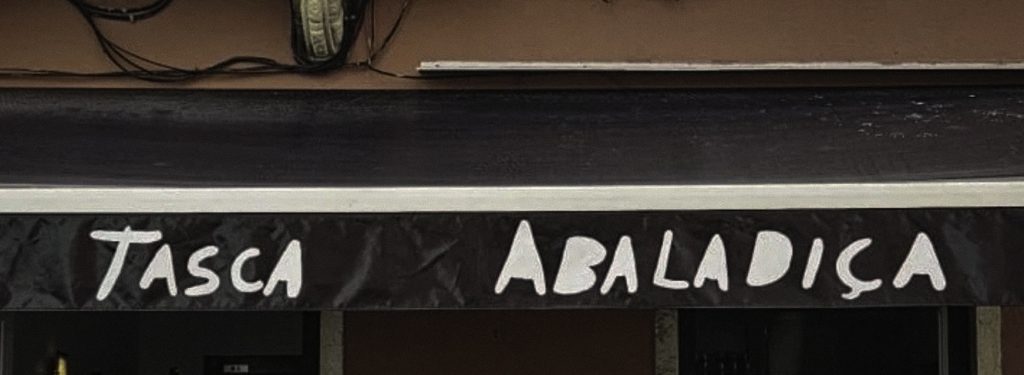 The exterior sign of Tasca Abaladiça, with the restaurant name hand-painted in white lettering on a dark background above the entrance.