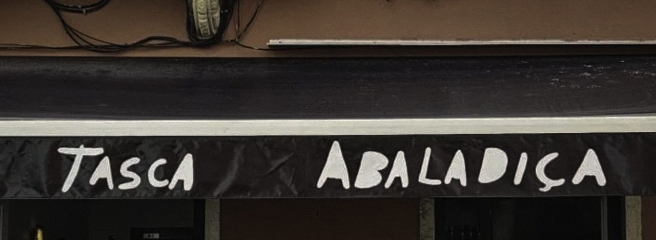 The exterior sign of Tasca Abaladiça, with the restaurant name hand-painted in white lettering on a dark background above the entrance.